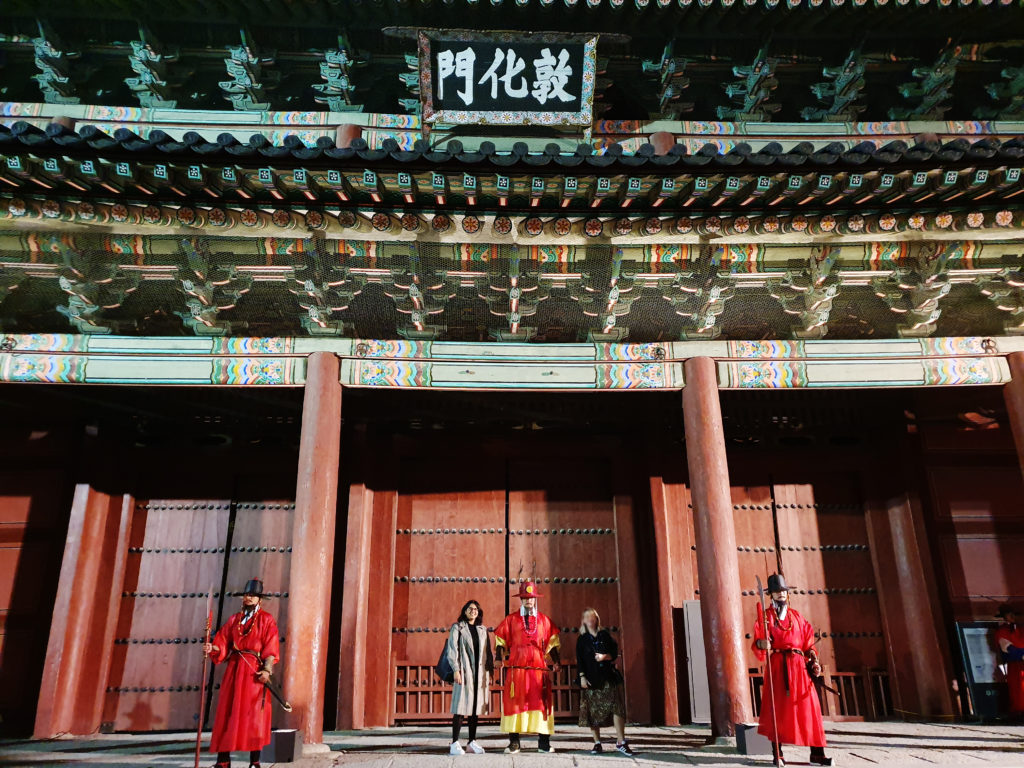 Picture shows two women standing with guards in front of Gyeongbokgung Palace